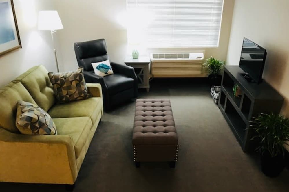 A cozy living room with a sofa, armchair, ottoman, and a lamp.