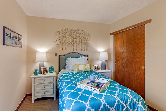 A cozy bedroom featuring a single bed with a blue patterned duvet, flanked by nightstands and lamps, accented with wall art.