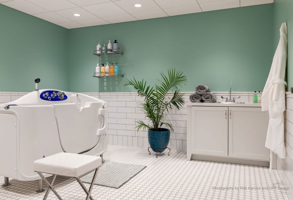 A modern bathroom with a walk-in tub, featuring green walls and sleek white tiles.