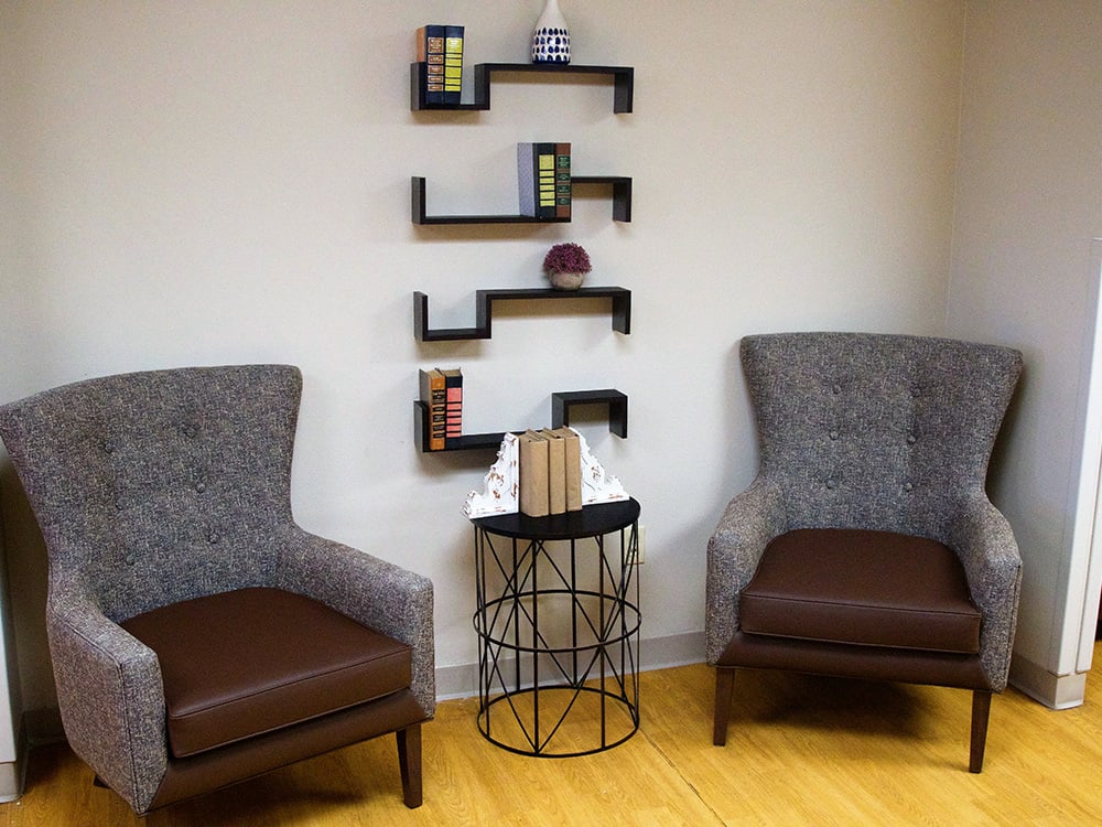 A modern living room with stylish zigzag shelves, comfortable chairs, and a decorative side table.