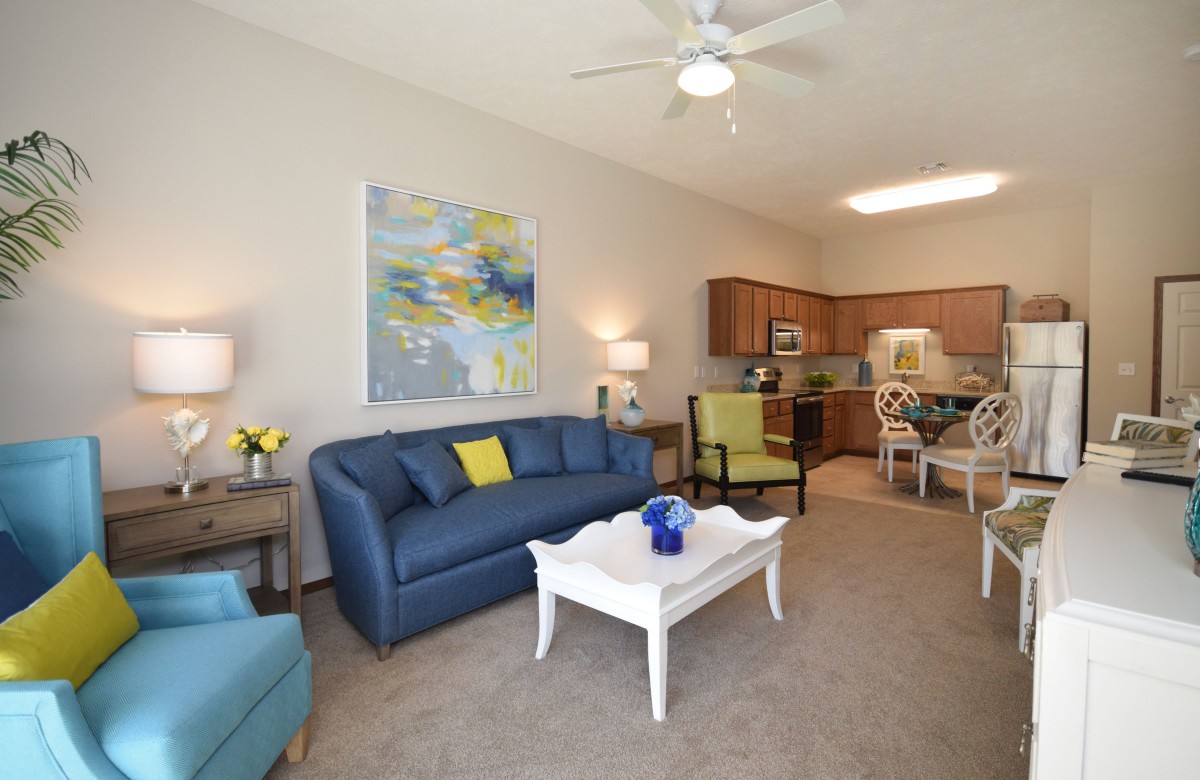 A modern living room with a blue sofa, white coffee table, and an open kitchen dining area.