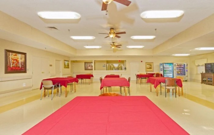 An indoor dining area with red tablecloths, tables and chairs, bright lighting, and ceiling fans.