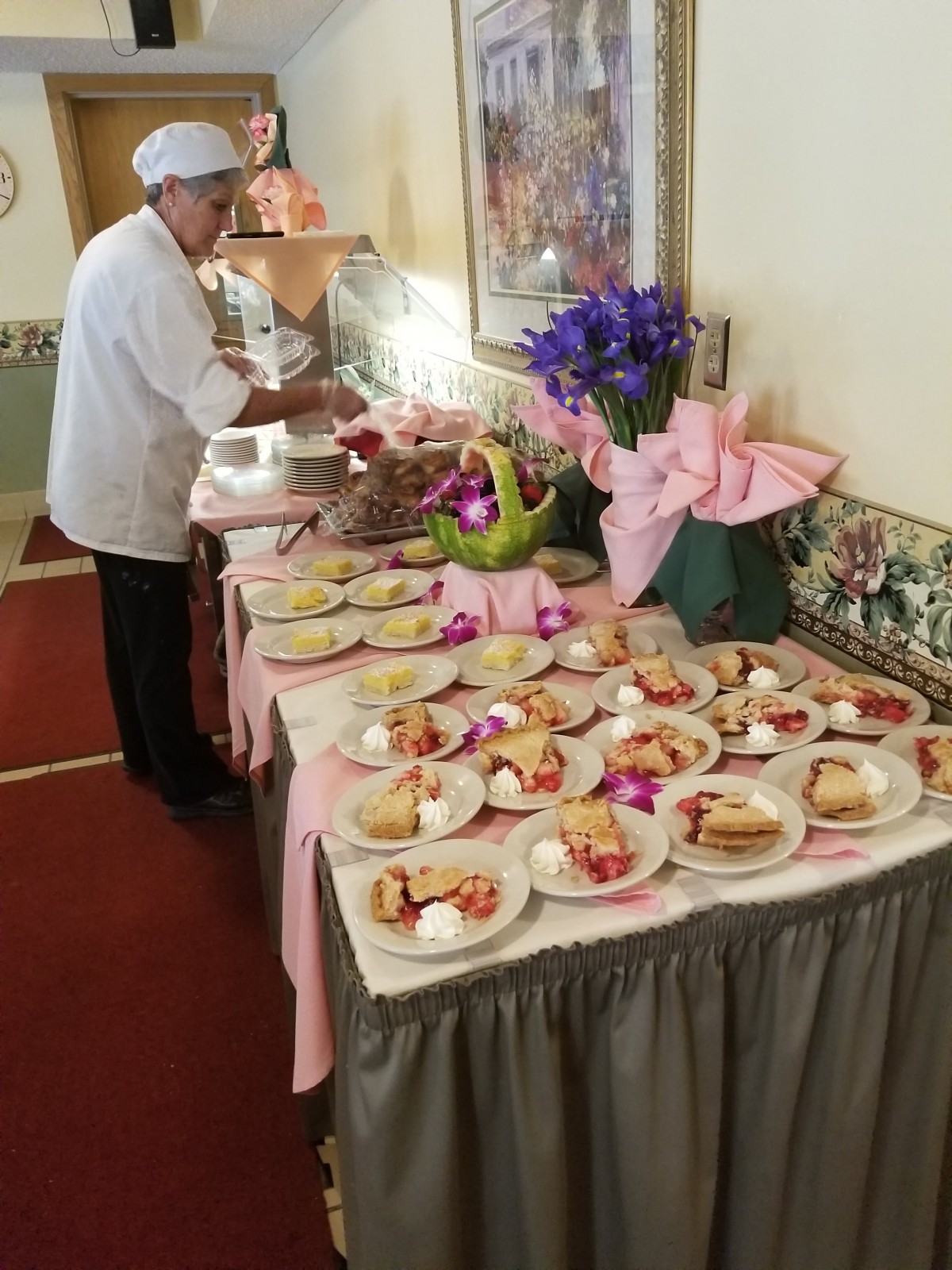 A chef prepares a buffet table adorned with desserts and decorative flowers.