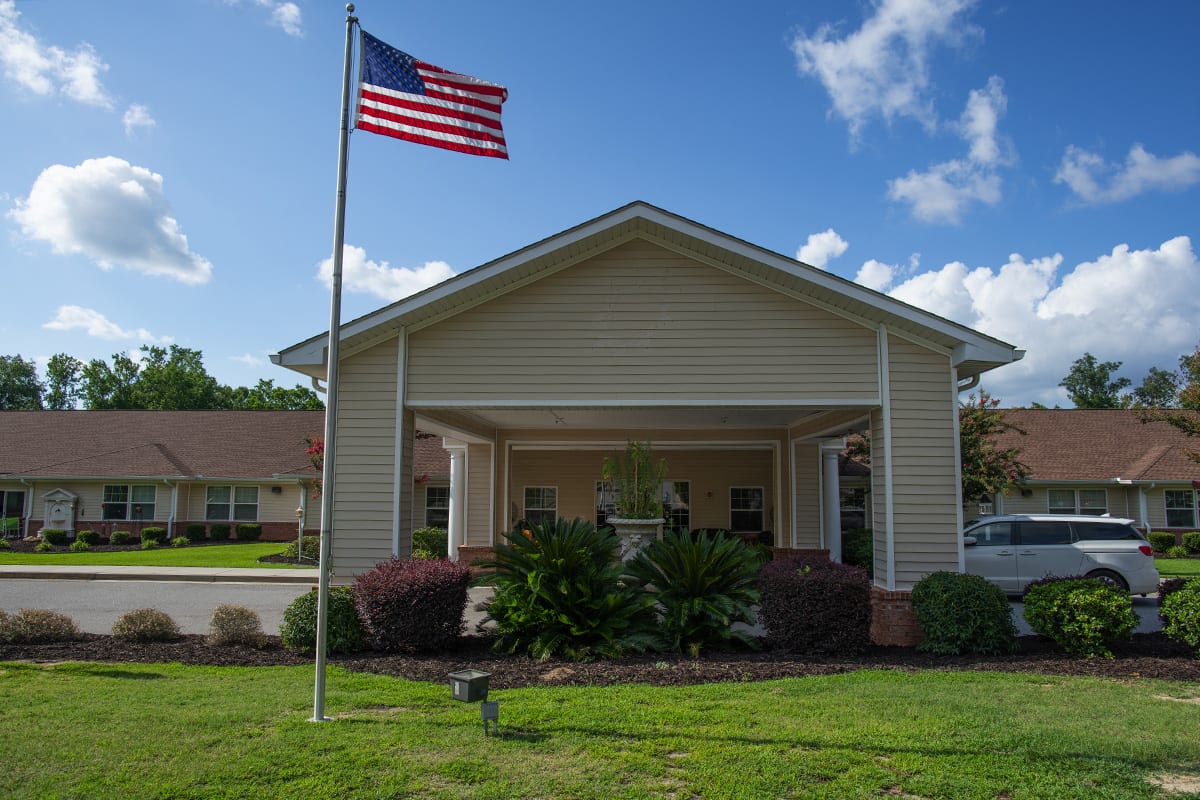 A house with a front porch and an American flag flying on the lawn under a blue sky.