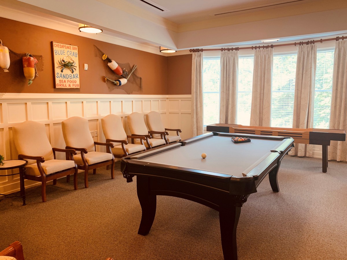 A cozy billiard room featuring a pool table, a row of chairs, and large windows allowing natural light.