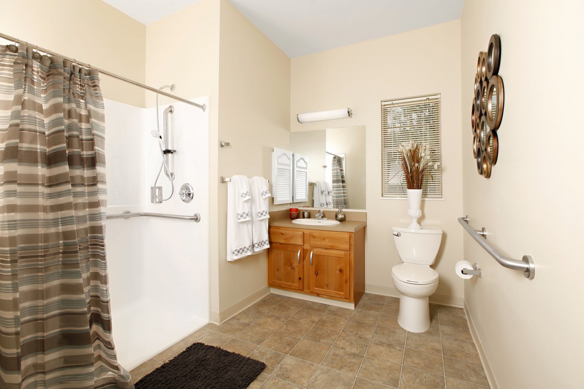 A modern bathroom featuring a shower area, toilet, and sink with wooden vanity.