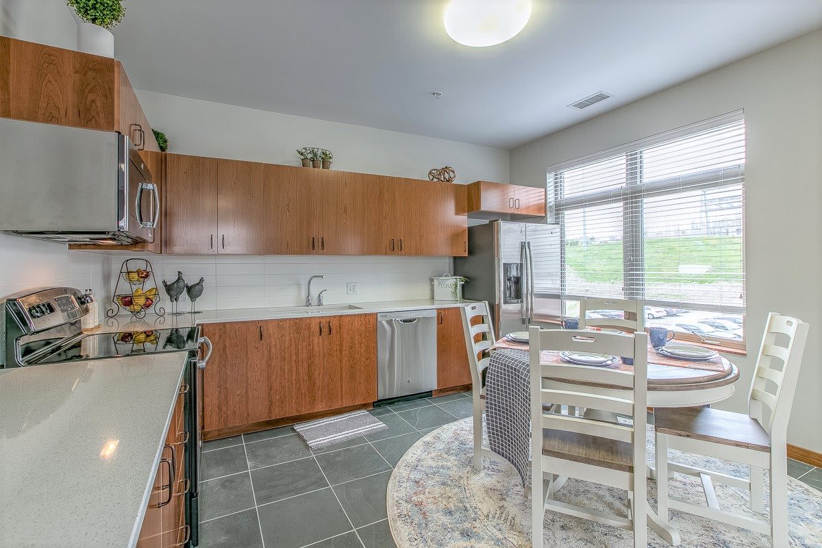 A spacious kitchen with wooden cabinets, modern appliances, and a dining area with a table and chairs, illuminated by natural light from large windows.