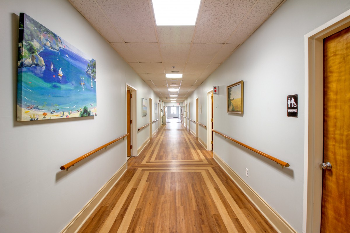 A well-lit hallway with wooden floors, lined with paintings on the walls.