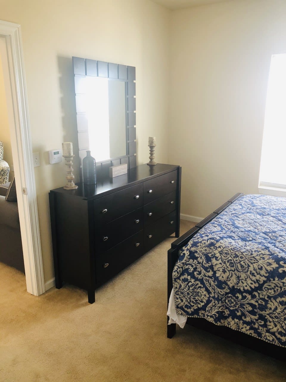 A cozy bedroom with a dresser and mirror beside a bed with patterned bedding.