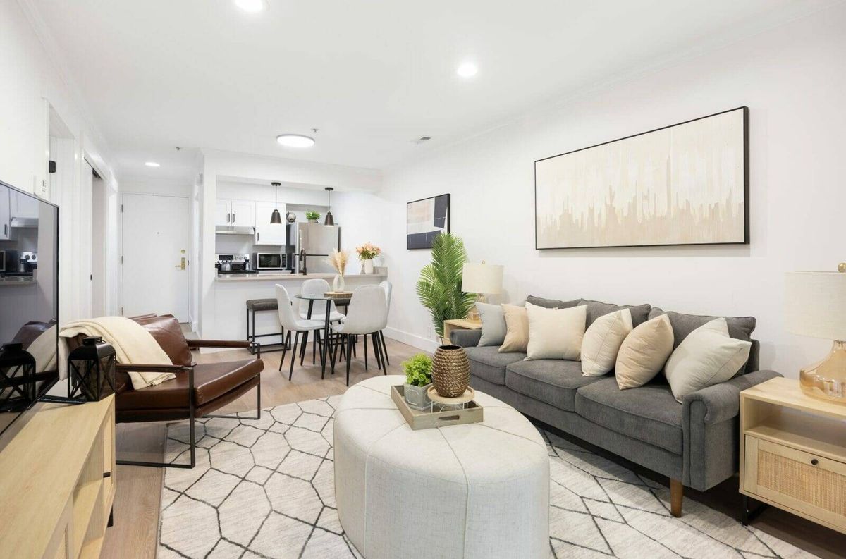 A modern living room with a stylish gray sofa, geometric coffee table, and elegant artwork, leading into a dining area.