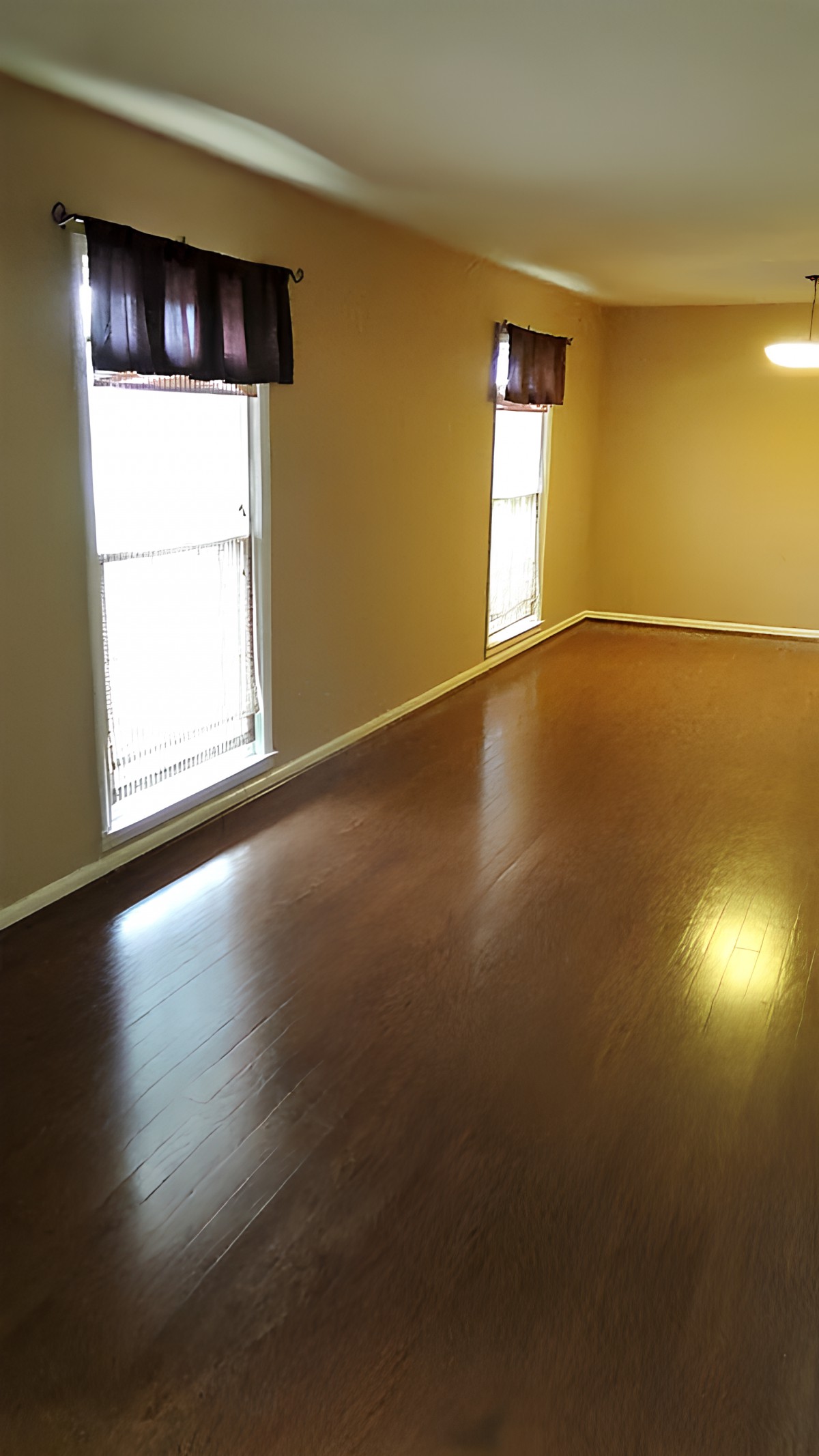 An empty room with hardwood flooring and two large windows.