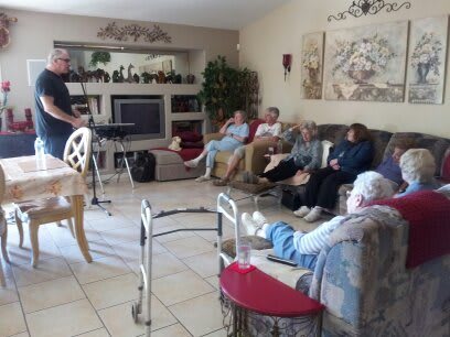 A group of people seated in a cozy living room, some with walkers nearby, watching TV.