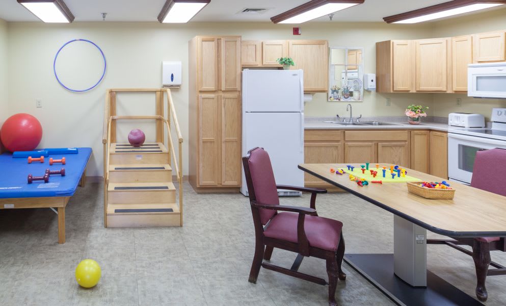 A therapy room in a rehabilitation center featuring indoor stairs, a kitchen area, and exercise equipment.