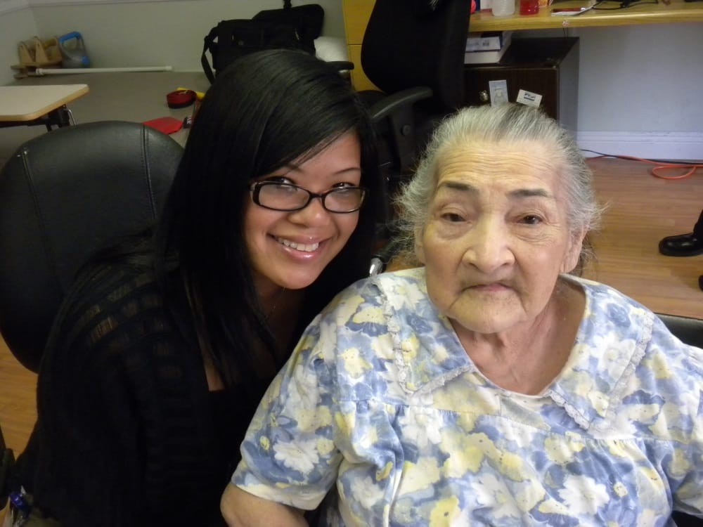 A young woman and an elderly woman sitting together, smiling indoors.