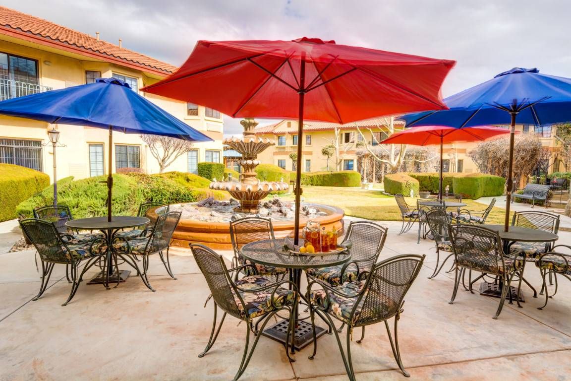 A picturesque patio with colorful umbrellas, tables, and chairs surrounding a central fountain.
