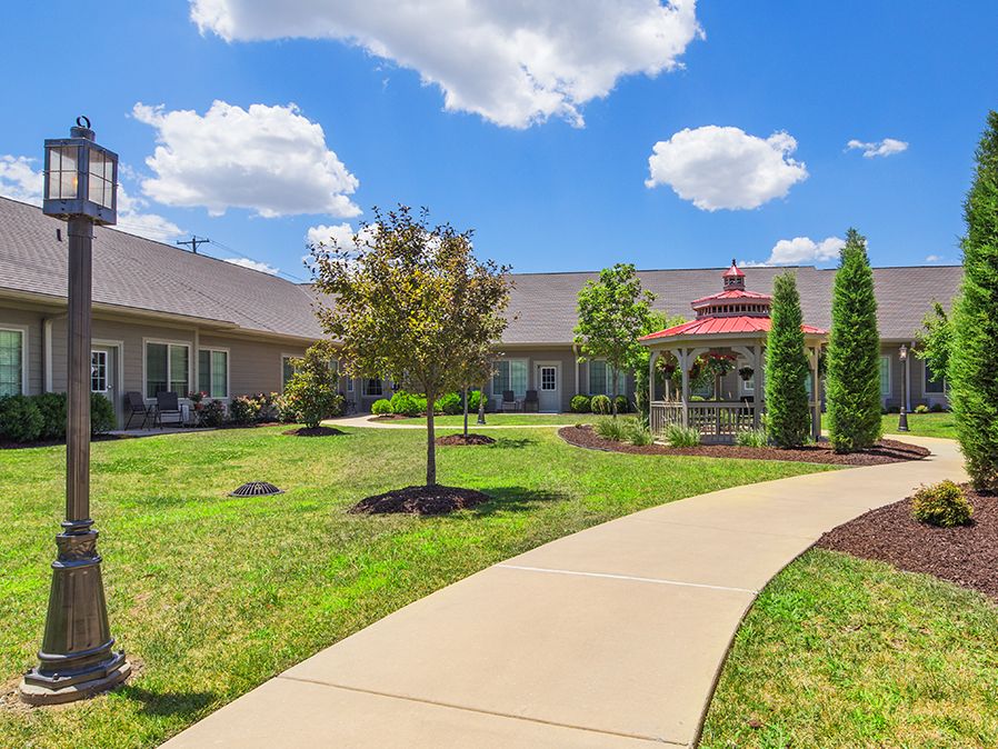 A scenic view of a landscaped garden with a pathway leading to a large building under a clear blue sky.