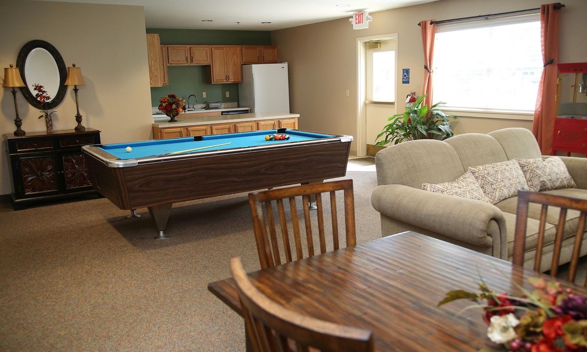 A cozy lounge area featuring a billiards table, kitchen, and comfortable seating.
