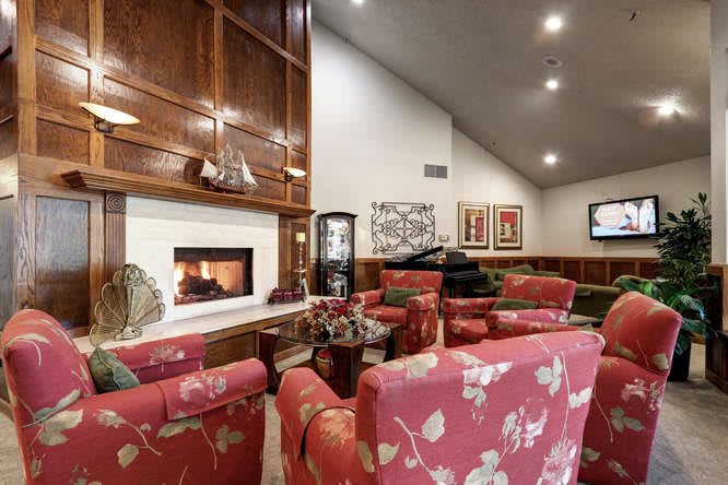 A cozy living room featuring a fireplace, floral armchairs, and elegant wood paneling.