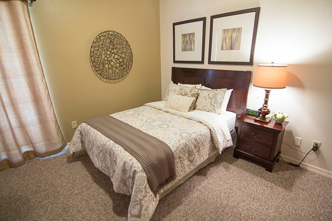 A cozy bedroom with a neatly arranged bed, nightstand, and decorative artwork.