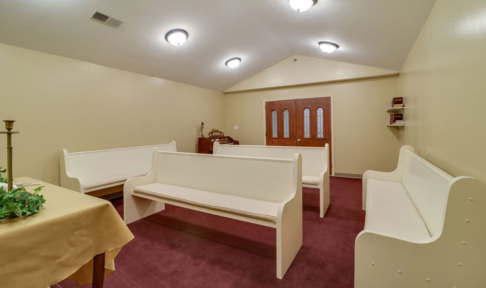 An interior view of a small church with white pews and carpeted flooring.