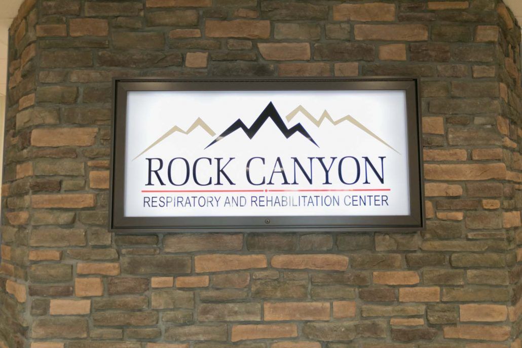 A sign for Rock Canyon Respiratory and Rehabilitation Center mounted on a stone wall.