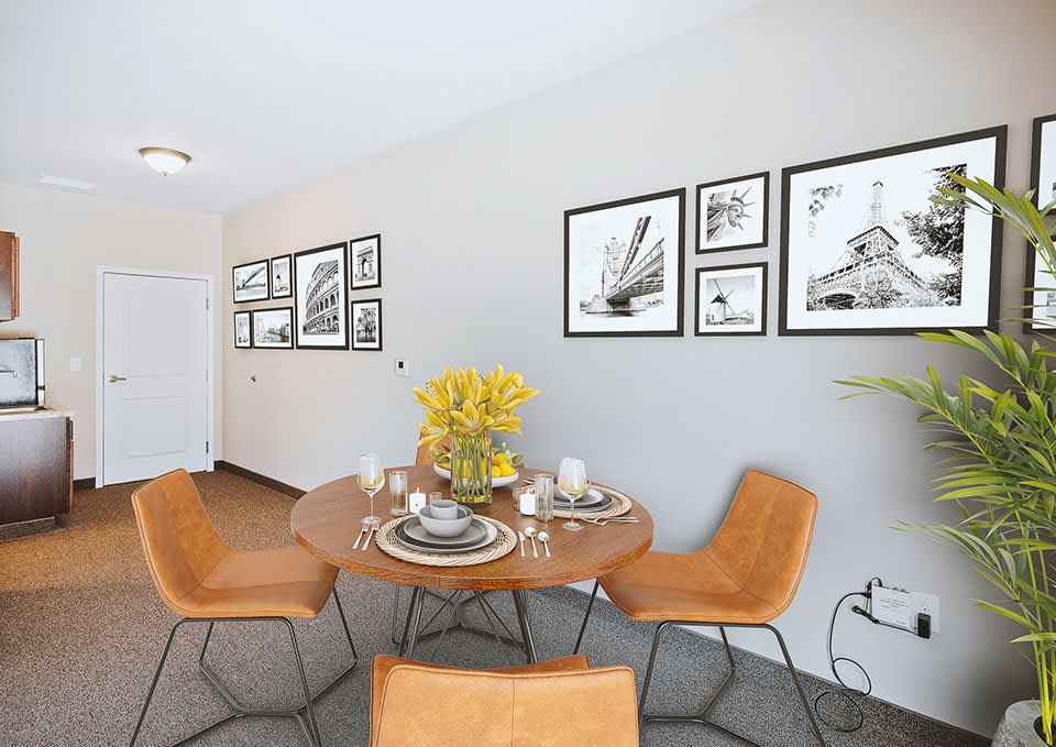 A modern dining room featuring a round wooden table with four leather chairs and framed artwork on the walls.