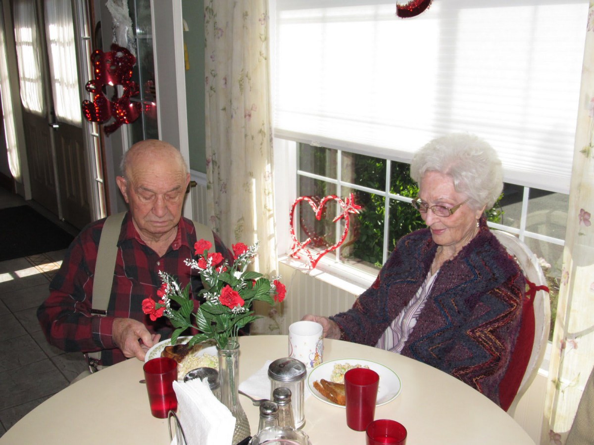 An elderly couple sitting at a table adorned with red Valentine's Day decorations and roses.
