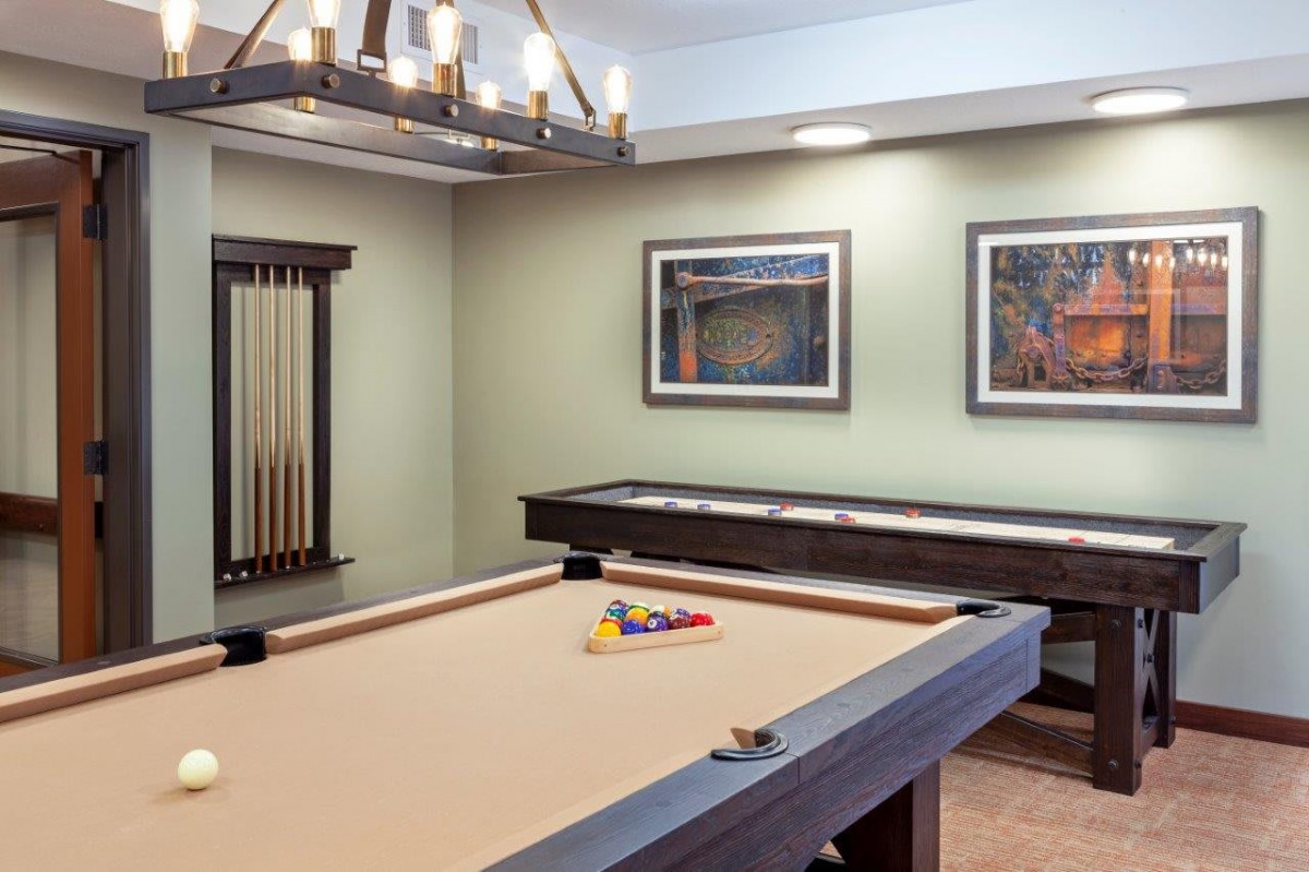 A stylish game room featuring a pool table and shuffleboard with elegant lighting and artwork on the walls.