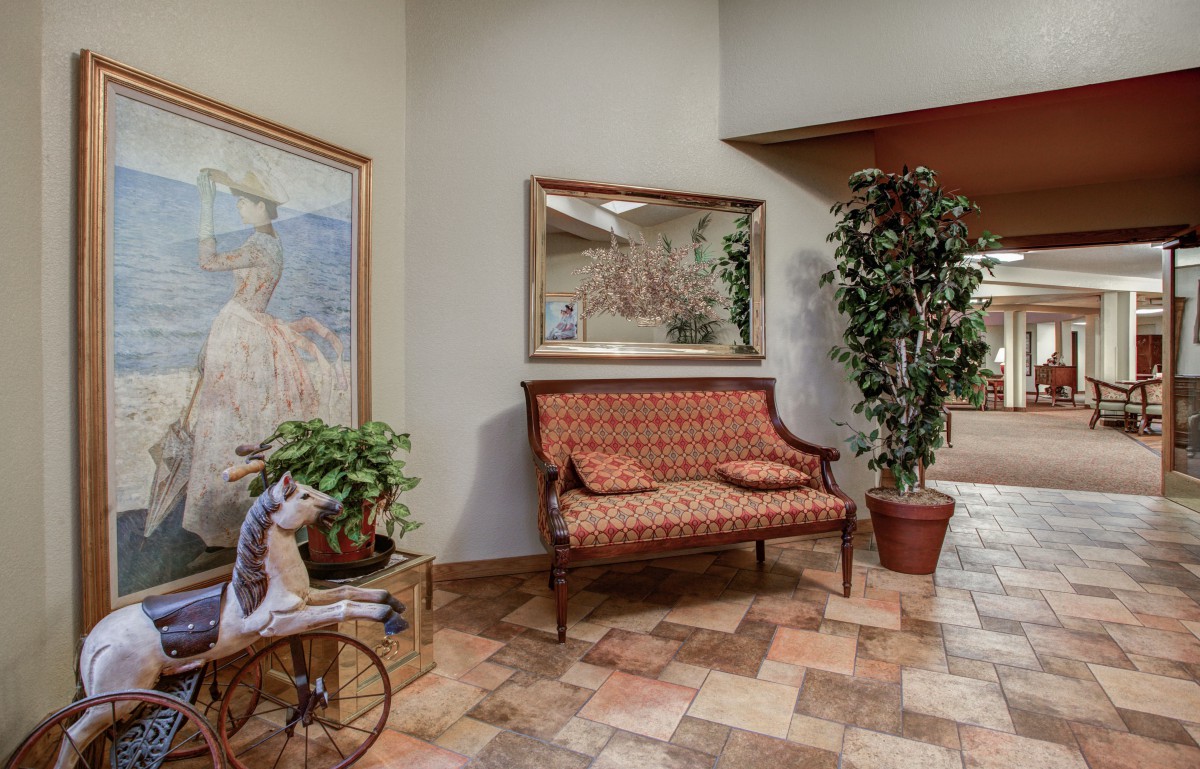 A cozy interior space featuring a patterned bench, a large mirror, potted plants, decorative artwork, and tiled flooring.