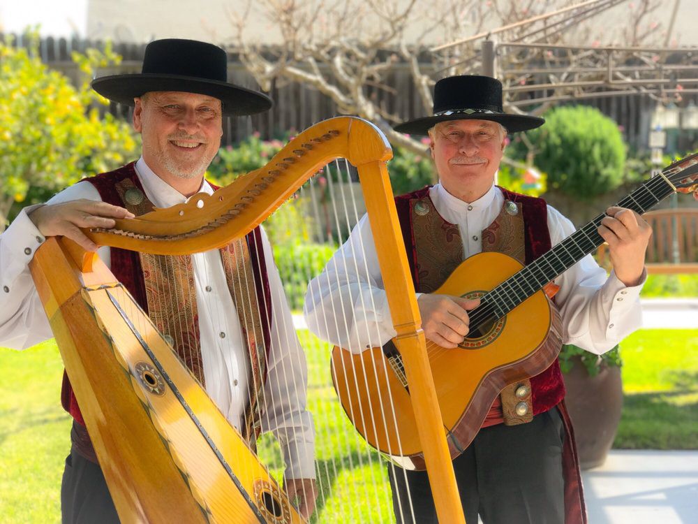 Two musicians in traditional attire playing the harp and guitar outdoors.