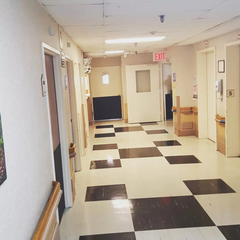 A hospital corridor with checkered flooring and several doors along the walls.