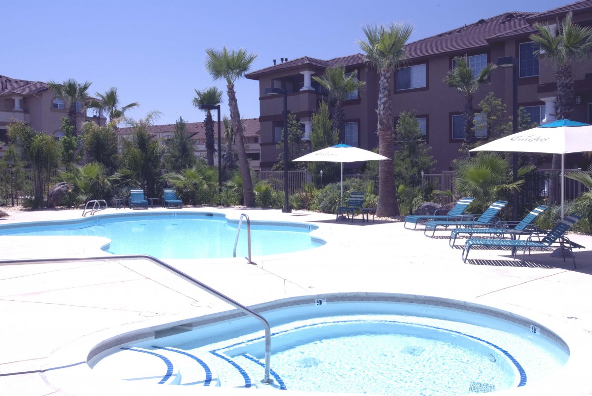 An outdoor pool area at an apartment complex with palm trees and lounge chairs.