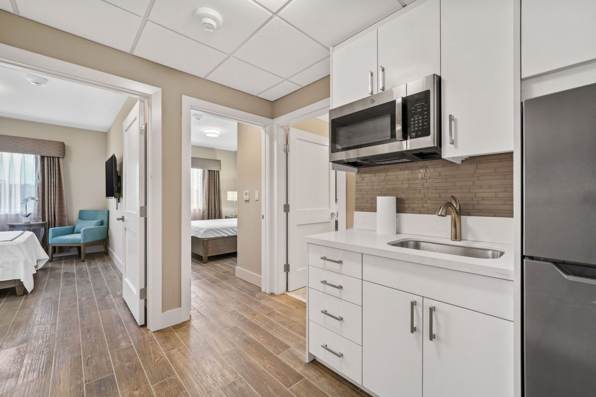 A modern kitchen area in an apartment with white cabinets, wood flooring, and a microwave.