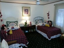 A cozy bedroom with twin beds featuring plaid bedding and decorative pillows, well-lit by a bedside lamp and adorned with wall art.