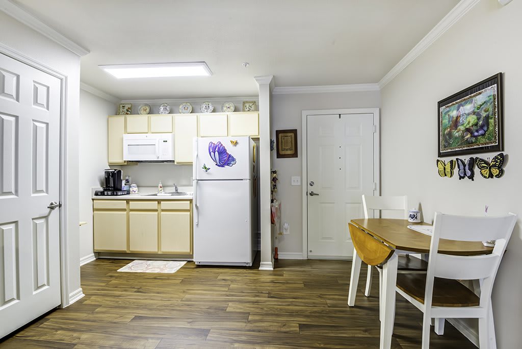 A compact apartment kitchen with a dining area, featuring light wood flooring and modern appliances.