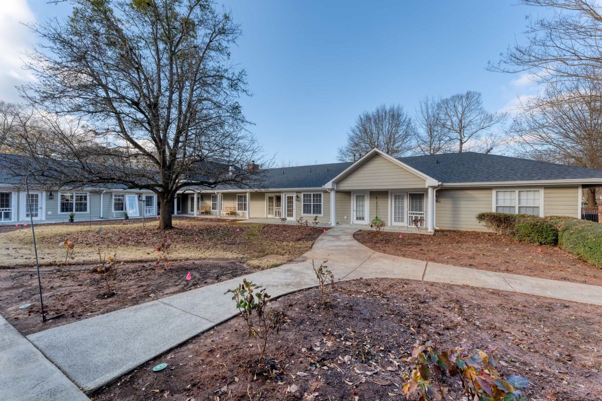 A suburban ranch-style house with a walkway leading to the entrance and trees in the front yard.