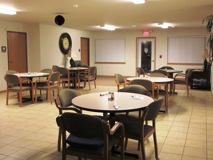 An empty dining area with round tables and chairs, softly lit by overhead lights.