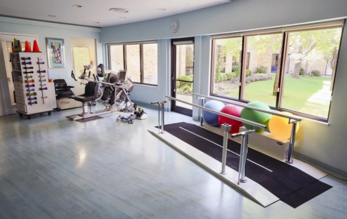 A spacious fitness room equipped with various exercise machines and therapy tools.