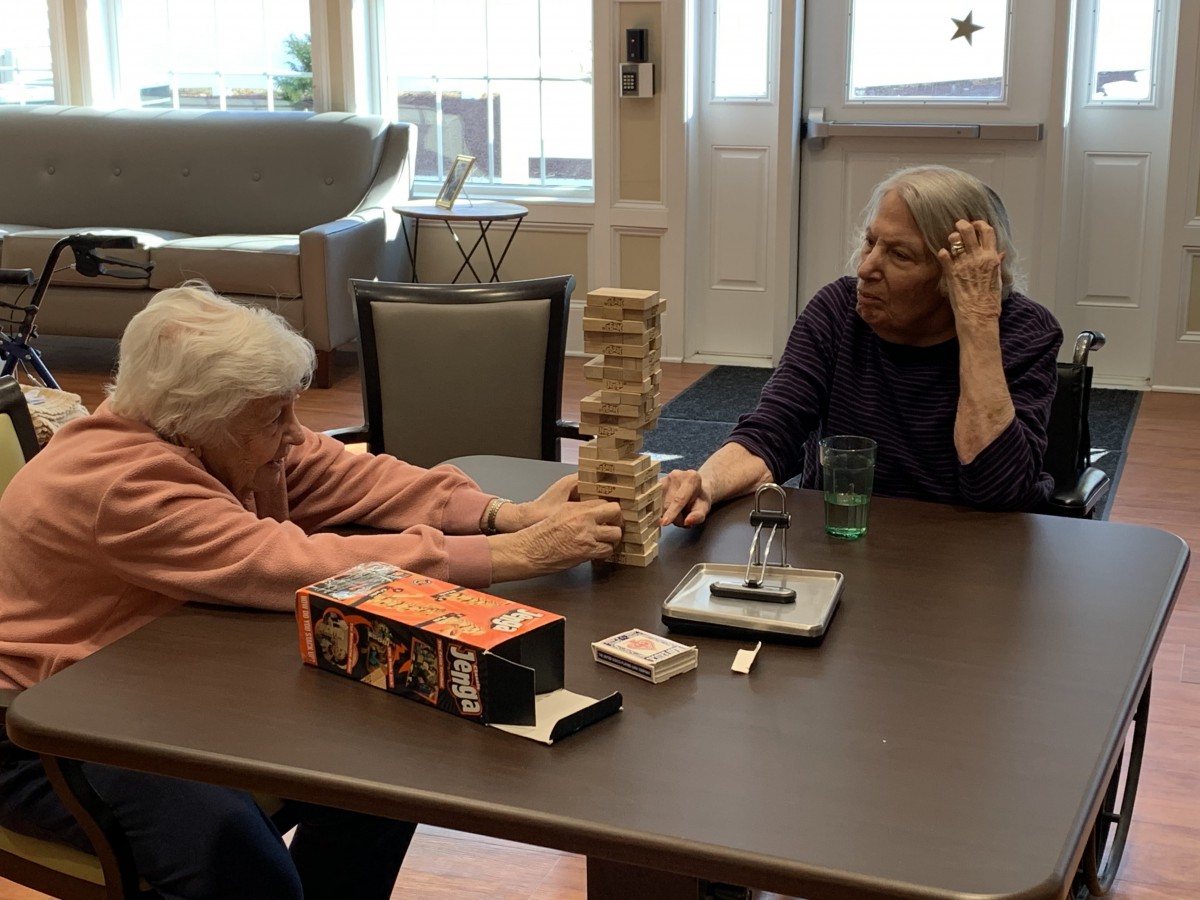 Two seniors playing Jenga at a table, enjoying a leisurely indoor activity.