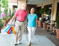 An elderly couple walking together while carrying shopping bags.