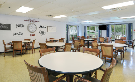 A spacious dining area featuring round tables and wooden chairs, illuminated by natural light.