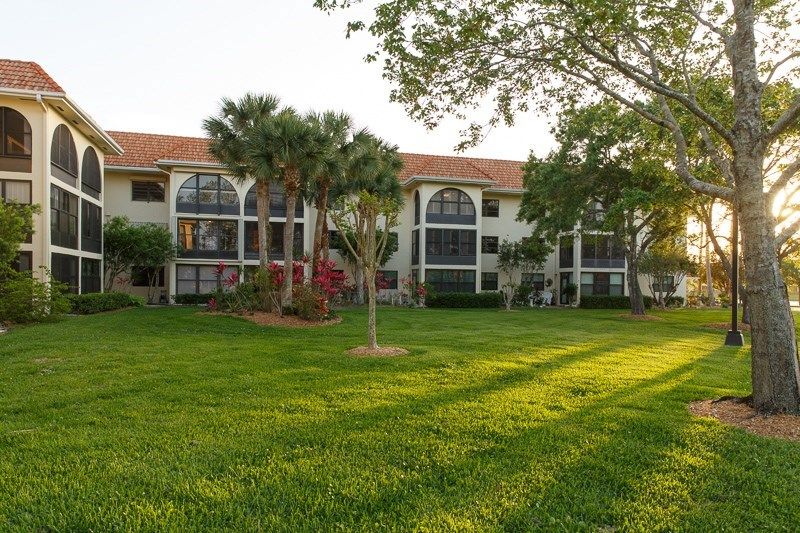 A scenic view of an apartment building surrounded by a lush green lawn and palm trees under warm sunlight.
