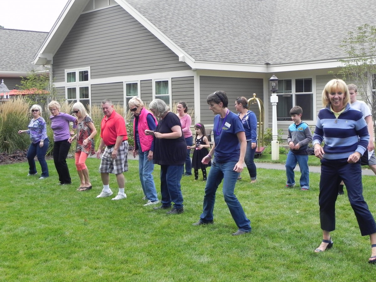 A group of people enjoying line dancing outside on the grass.