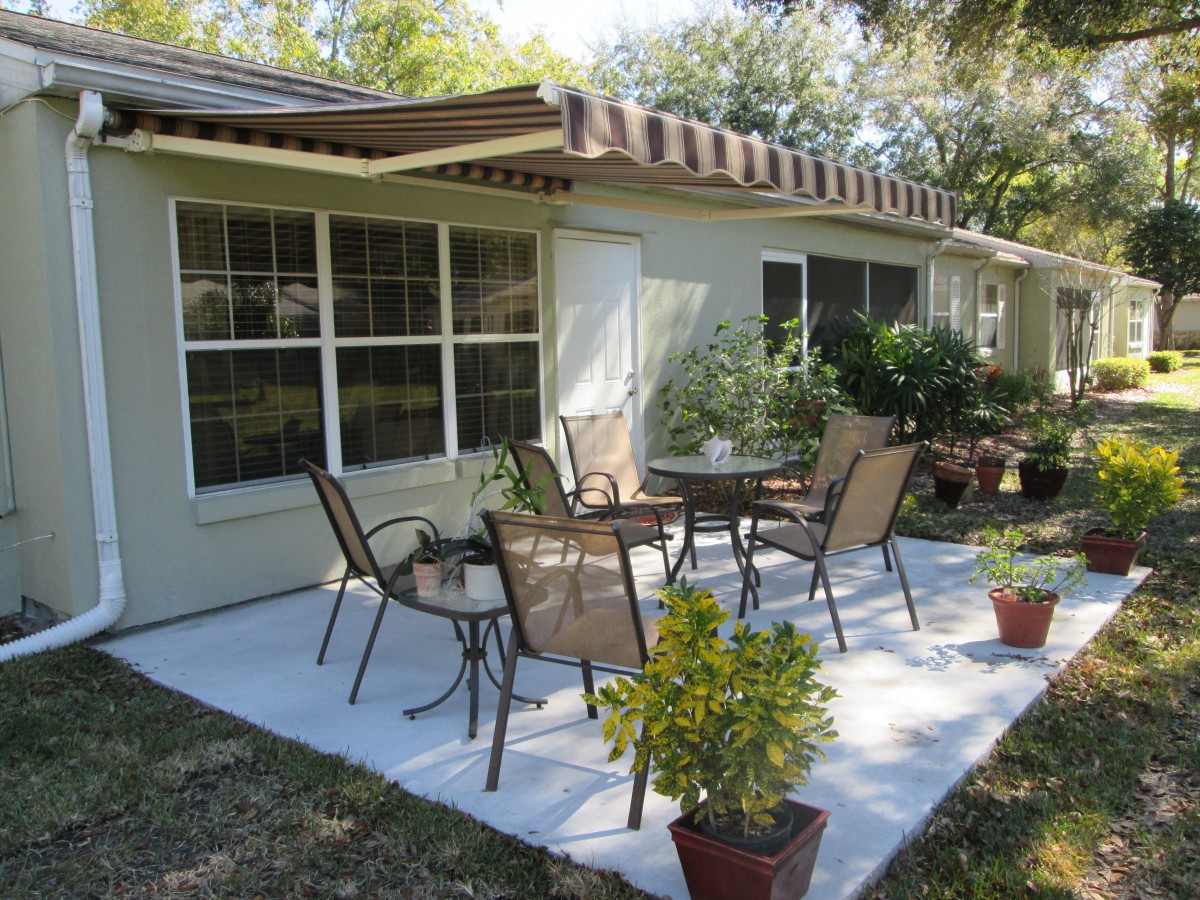 A cozy backyard patio with chairs and a table surrounded by potted plants.