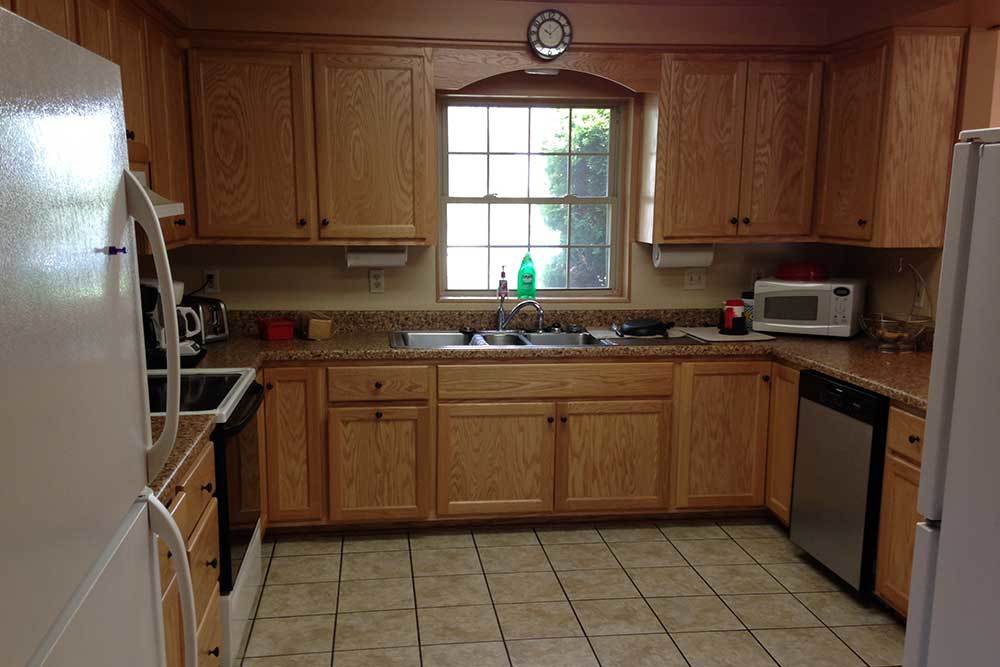 A spacious kitchen featuring wooden cabinets, a central window above the sink, and essential appliances.