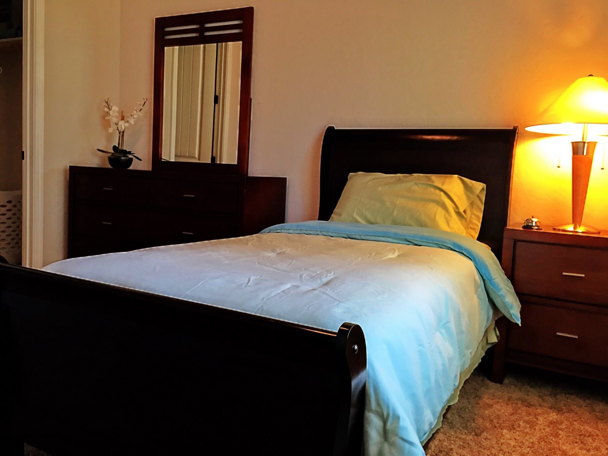 A cozy bedroom with a single bed, dresser, and warm lighting.