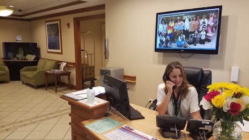 A receptionist attending to a call at the front desk of an office, with a monitor displaying a group photo.