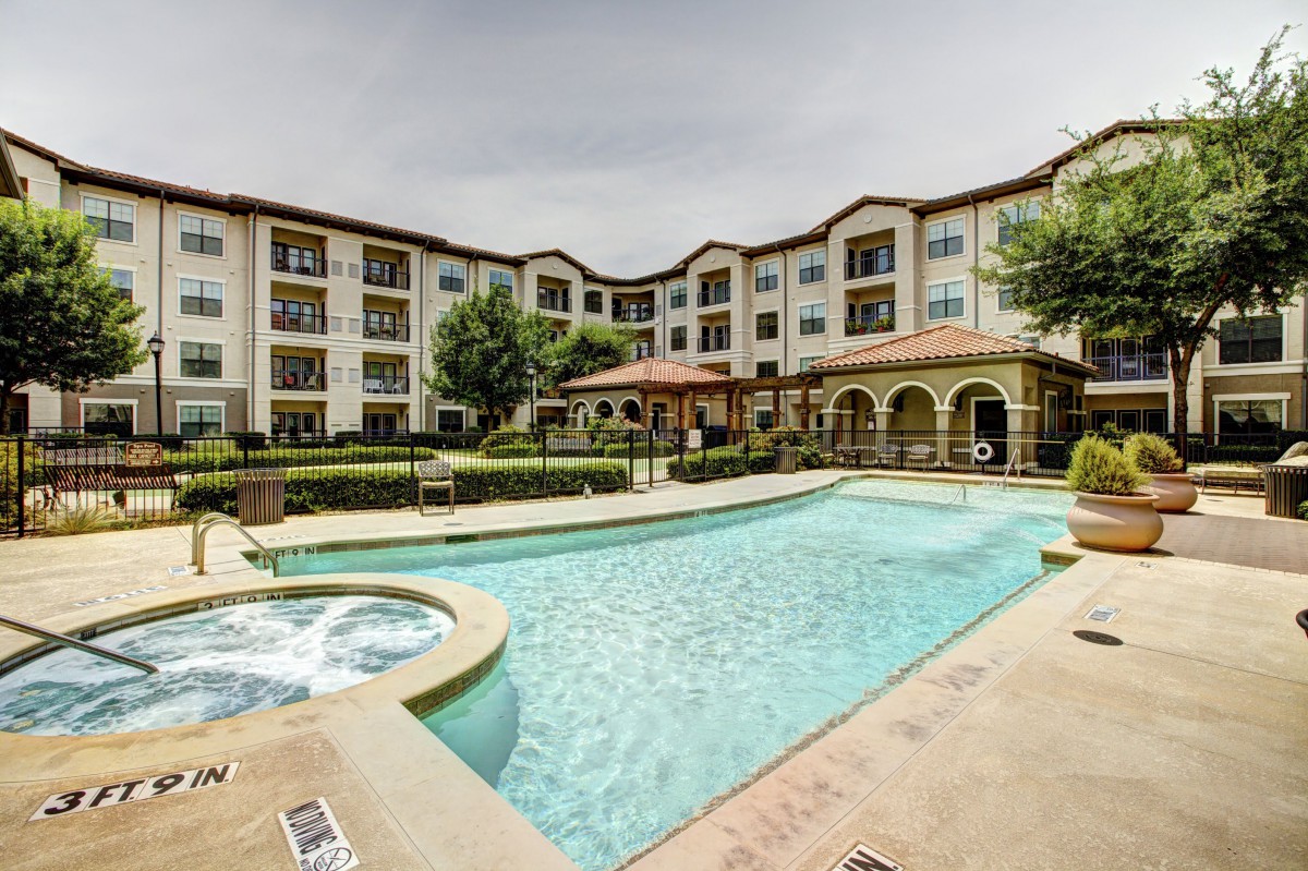 A residential apartment complex with a large outdoor swimming pool and landscaped surroundings.