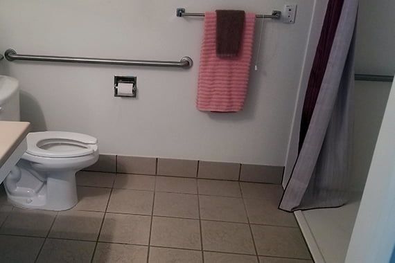 A bathroom with a toilet, grab bar, hanging towels, and a tiled floor.