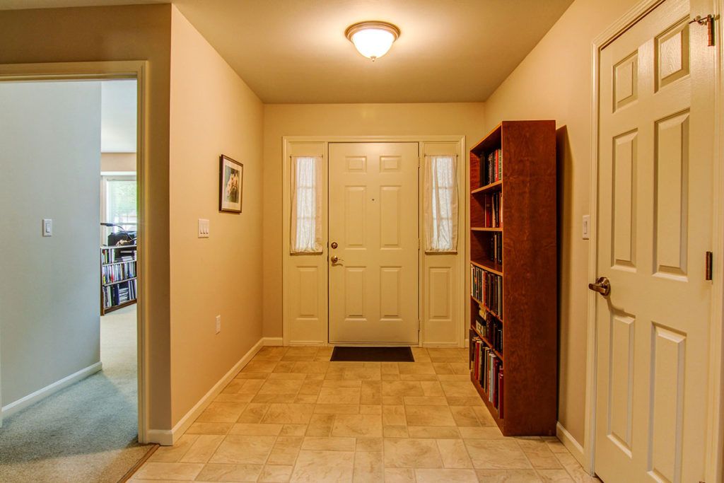 A well-lit entryway featuring a front door with glass panels, a wooden bookshelf, and tiled flooring.